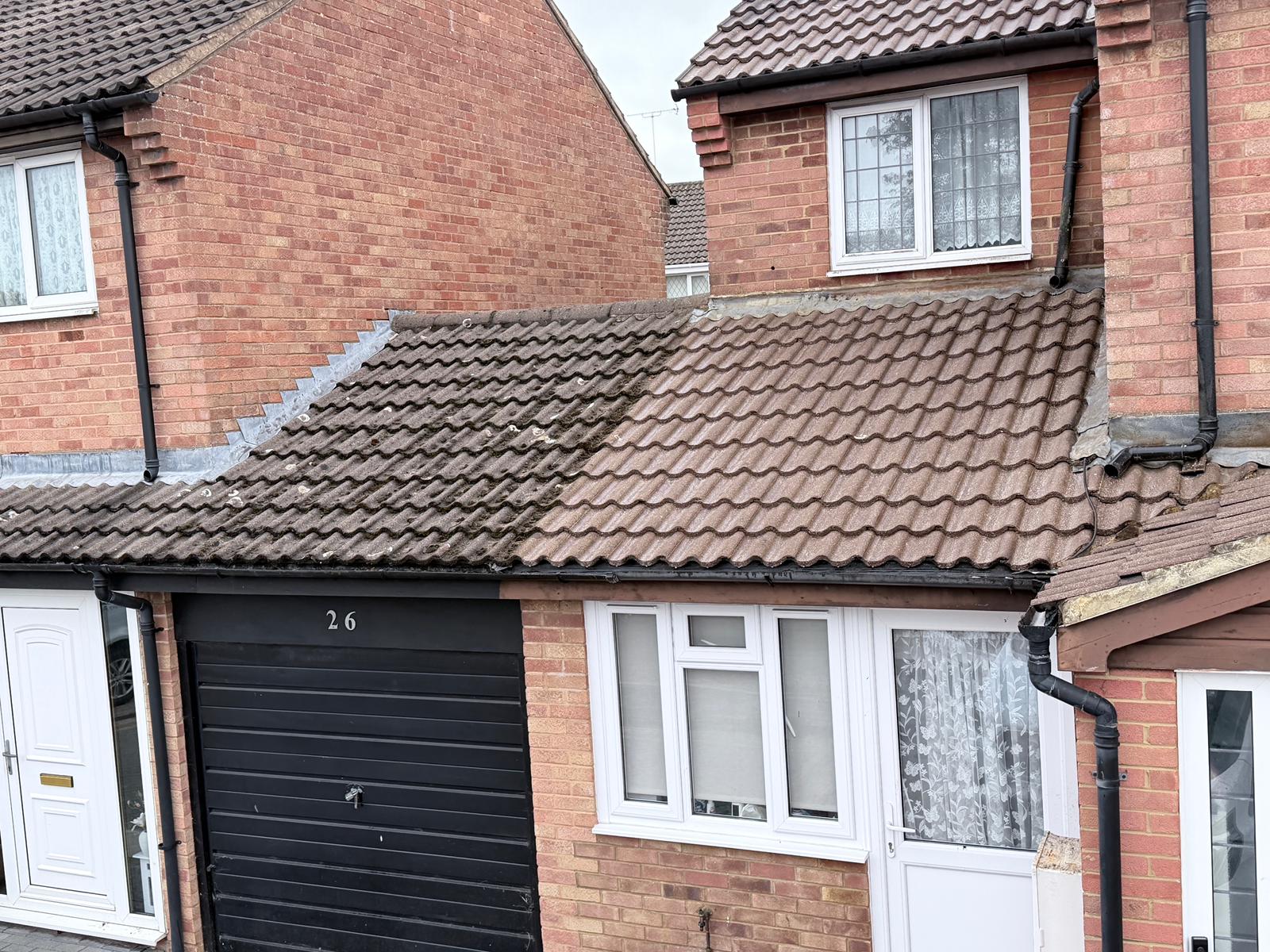 A brick house with a black garage door numbered 26, its extension and garage roof covered in freshly cleaned red-brown profiled tiles between neighbouring brick walls.
